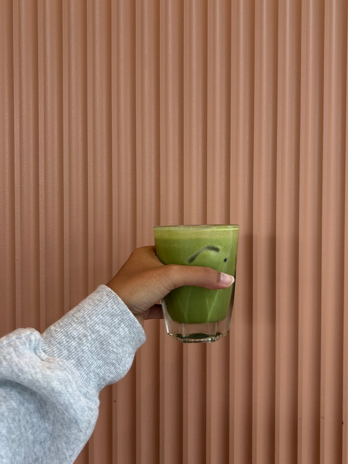 Hand holding an iced matcha drink against a warm paneled wall