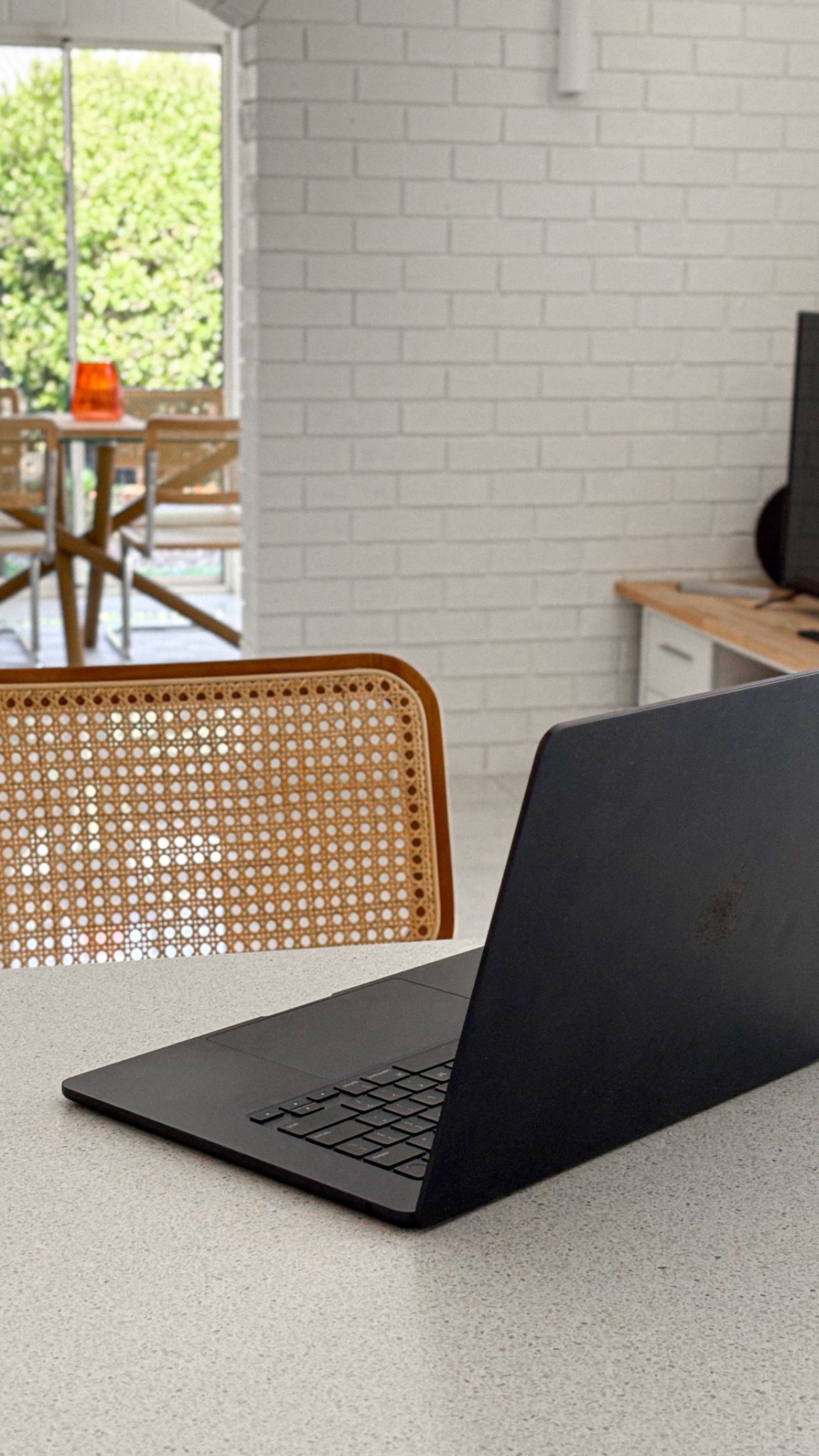 Laptop on a bright table beside a cane chair