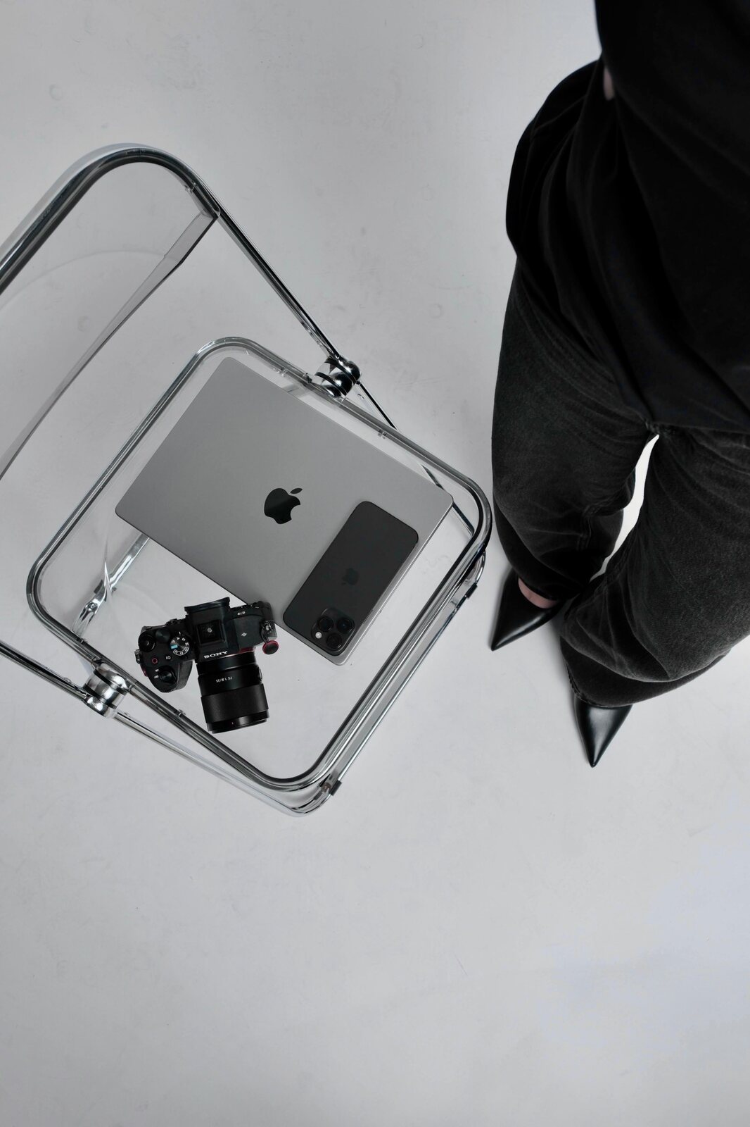 Clear chair holding a camera, laptop and phone beside a standing creative
